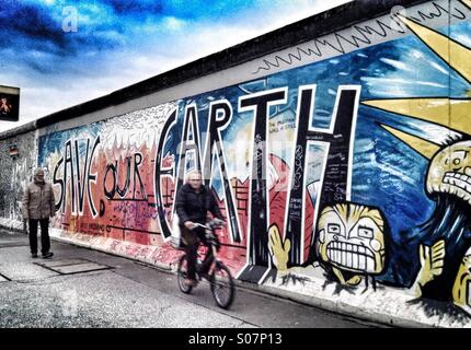 'Save notre terre". Les cycles d'un homme passé un reste du mur de Berlin qui a été peint avec un message sur l'environnement Banque D'Images