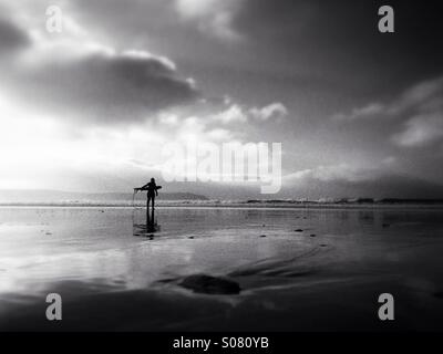 Lone surfer carrying sa planche de surf sur la plage de Woolacombe North Devon, Angleterre Banque D'Images