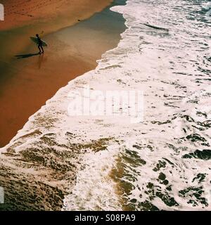 Un surfeur mâle s'approche de la plage. Manhattan Beach, Californie, États-Unis. Banque D'Images