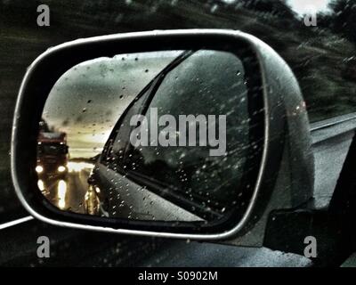 Voir dans le rétroviseur de voiture de lointains phares et camion sur la route. Banque D'Images