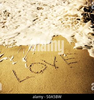 Amour écrit dans le sable avec une vague s'écraser. Manhattan Beach, Californie, États-Unis. Banque D'Images