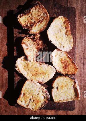 Tranches de pain au levain beurré sur une planche à découper en bois. Banque D'Images