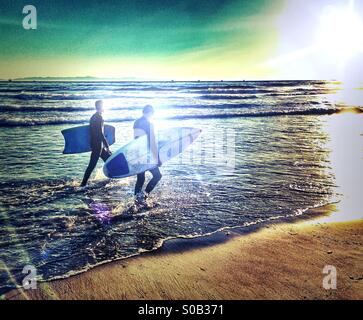 Deux jeunes surfeurs à pied le long de la plage au coucher du soleil après le surf sur une chaude journée d'hiver en Californie Banque D'Images