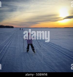 Un ski familial sur les voies d'un lac gelé lors d'une maison de vacances dans l'Arctique scandinave nordique Finlande au coucher du soleil Banque D'Images