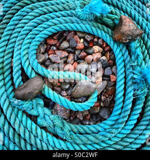 Une bobine de corde bleu bateau sur une plage décrivant la forme d'un neuf et maintenu en position par des pierres et cailloux Banque D'Images