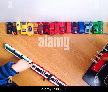 Toy cars alignés dans les couleurs arc-en-ciel avec un bébé garçon jouant avec un tramway à côté d'un garage de stationnement Banque D'Images