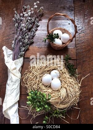 Composition de pâques rameaux de saule à chatons, buis, des oeufs dans un panier de Pâques et la paille nid, situé sur la vieille table en bois. Chatons sont enveloppé dans du papier Banque D'Images