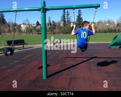 Garçon sur swing sur jeux pour enfants au parc Banque D'Images