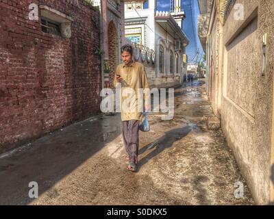 Man texting on mobile phone pendant qu'il marche dans la rue , Kharian village Pakistan Banque D'Images