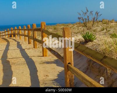 Chemin de sable - une clôture en bois protégeant une dune de sable s'étend jusqu'à la plage de sable fin avec la mer bleu foncé et ciel bleu au-delà ! Prise à Ocean City, NJ (USA) par un beau jour de printemps. Banque D'Images