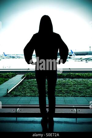 Silhouette de jeune femme aux cheveux longs désireux d'être sur son chemin comme elle regarde pensivement vers la piste de l'aéroport et du ciel Banque D'Images