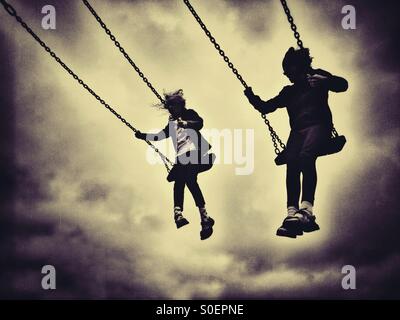 Deux filles sur des balançoires en silhouette contre le ciel nuageux Banque D'Images