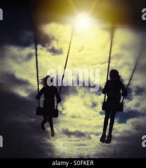 Deux filles sur des balançoires en silhouette contre le soleil du soir Banque D'Images