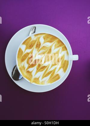 Vue de dessus de tasse de café avec soucoupe et cuillère sur fond violet. Banque D'Images