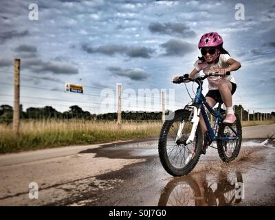 Girl having fun riding bicycle dans une flaque. Banque D'Images