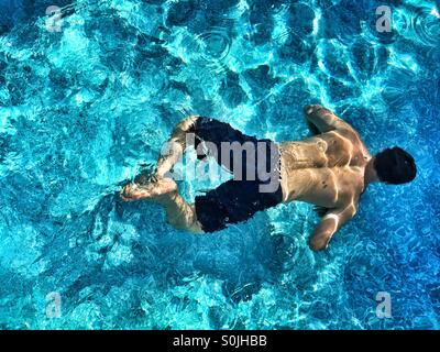 Jeune homme nage sous l'eau dans une piscine découverte sur une journée ensoleillée. Photo prise d'en haut. Banque D'Images