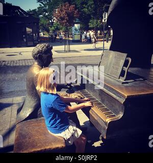 Petite fille assise à côté de la statue d'un célèbre compositeur polonais Moniuszko, sur la rue Piotrkowska de Łódź, Pologne, en faisant semblant de jouer son piano à ses côtés Banque D'Images