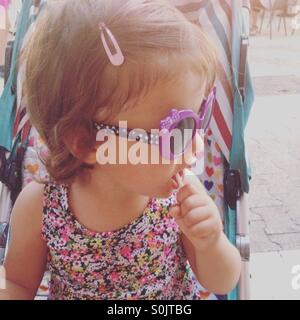 Petit bébé fille avec des lunettes de soleil et à la sucette sur le côté Banque D'Images