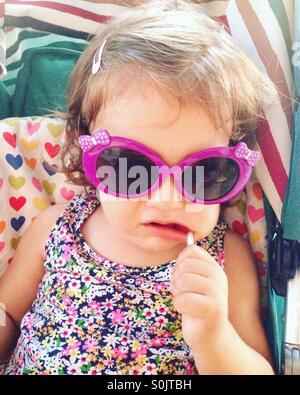 Baby Girl with lollipop et lunettes looking at camera Banque D'Images