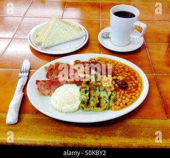 Petit-déjeuner anglais complet avec du bacon frit oeufs saucisse haricots et mug de café noir Banque D'Images