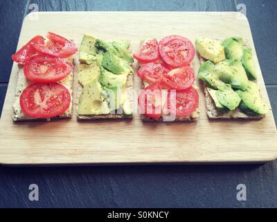 Les tomates et d'avocat des craquelins avec du hoummos sur une planche en bois Banque D'Images