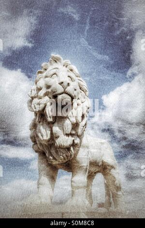 Une statue en pierre d'un lion debout fièrement sur un socle avec un bleu, ciel nuageux derrière. Banque D'Images