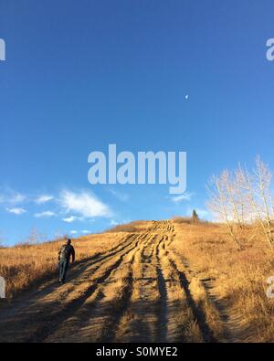 Homme marchant côte raide jusqu'à l'automne, avec le ciel bleu et le matin lune. Banque D'Images