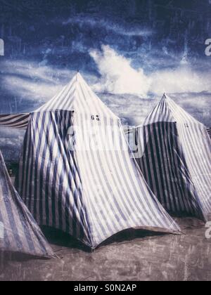 Plage rayé bleu et blanc tentes assis sur une plage de sable fin prêt pour les vacanciers. Banque D'Images