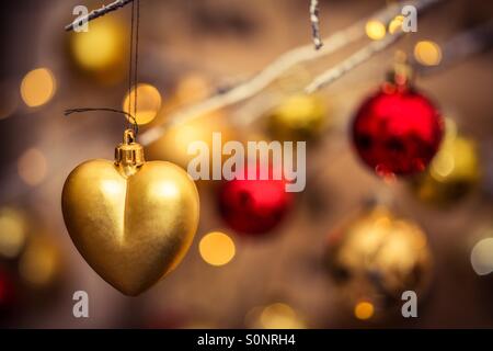 Décoration de Noël en forme de coeur en or accroché contre un joli flou d'arrière-plan coloré Banque D'Images