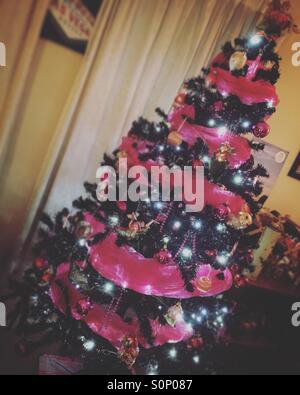 Arbre de Noël illuminé et orné de babioles et rose Banque D'Images