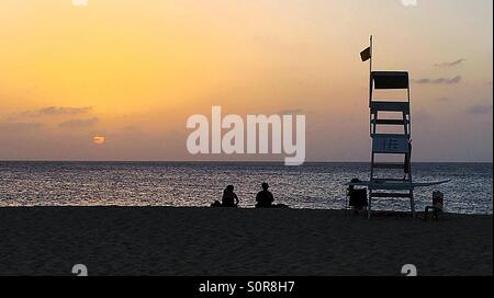 Silhouettes sur une plage au coucher du soleil avec l'océan qui mène à l'horizon Banque D'Images