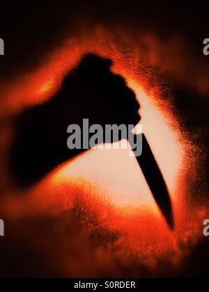 Ombre de bras tenant un couteau sur un fond rouge sang Banque D'Images