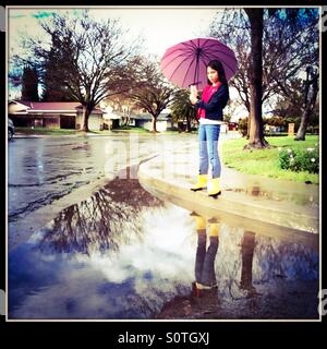 Une jeune fille de 12 ans avec des bottes de pluie et parapluie, la pluie s'éclaircit. Banque D'Images