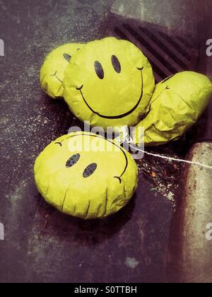 Triste, visage heureux dégonflé pose de ballons dans une flaque d'eau sur le côté de la rue Banque D'Images