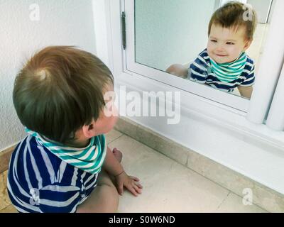 Cute smiling baby boy en se regardant dans un miroir Banque D'Images