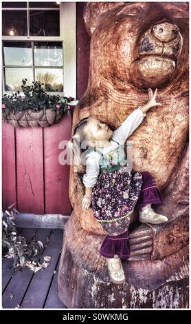 Petite fille assise sur un ours en bois sculpté Banque D'Images