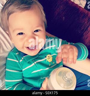 Baby Boy wearing green stripe pyjama, tenant une bouteille de lait, assis sur sa pierre tours, smiling at the camera Banque D'Images