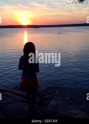 Silhouette de jeune fille au coucher du soleil en été sur un lac. Banque D'Images