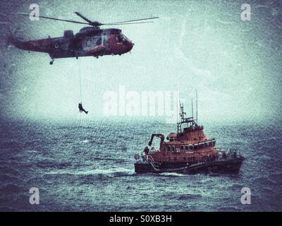 Un hélicoptère de sauvetage de la Marine royale d'une descente sur un canot de sauvetage de la RNLI pendant une tempête. Banque D'Images