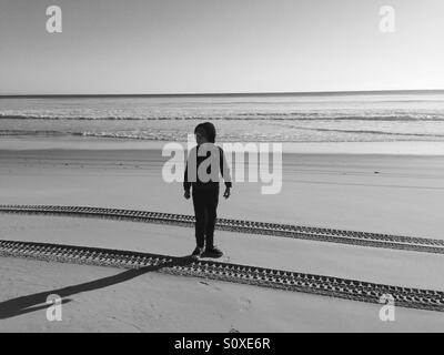 Photo en noir et blanc boy standing on beach at sunrise Banque D'Images