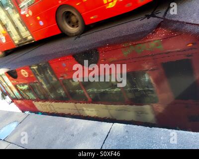 Reflet d'un bus à impériale, dans une flaque, après la pluie. Londres, R.-U. Banque D'Images