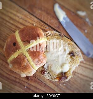 Hot cross bun coupé en deux et grillé au repos beurré sur la vieille planche à découper en bois. Banque D'Images