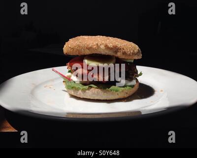 Maison d'alléchantes cheeseburger avec bacon, fromage mozzarella, tomates, concombres, laitue, dans un petit pain au sésame. Banque D'Images