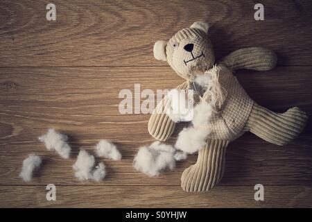 Un petit ours en peluche portant sur un sol en bois avec sa farce déchiré et tiré. Banque D'Images