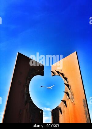 Seagull flying par rusty moderne sculpture sur la promenade sud de Blackpool Banque D'Images