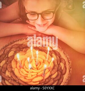 Petite fille avec des lunettes à son anniversaire à tarte avec 8 bougies. Banque D'Images