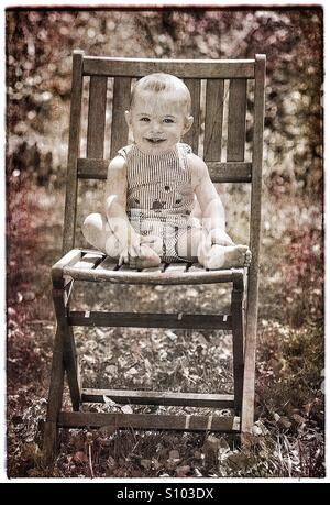 Bébé avec grand sourire assis sur une chaise à l'extérieur. Banque D'Images