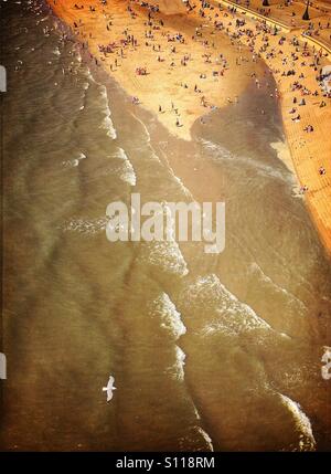Mouette volant au-dessus de la mer marée monte avec les gens entassés sur la plage à Blackpool Banque D'Images