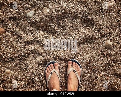 POV. Pieds en tongs sur la plage de galets Banque D'Images