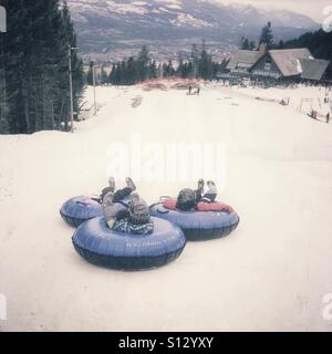 Trois enfants commencent leur glisser sur une colline sur innertubes. Banque D'Images